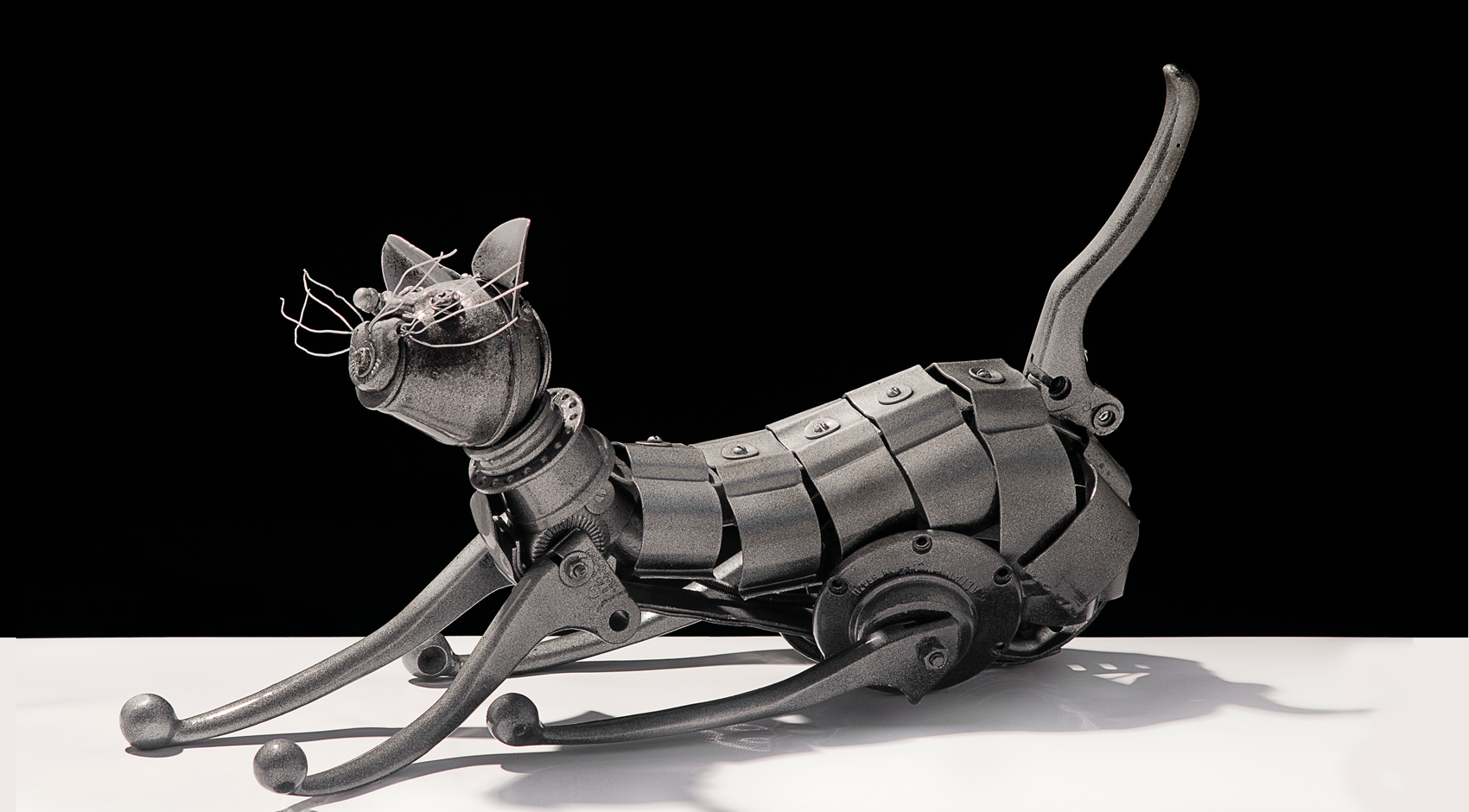 Escultura de um gato montada com peças de metal reaproveitado sobre fundo preto